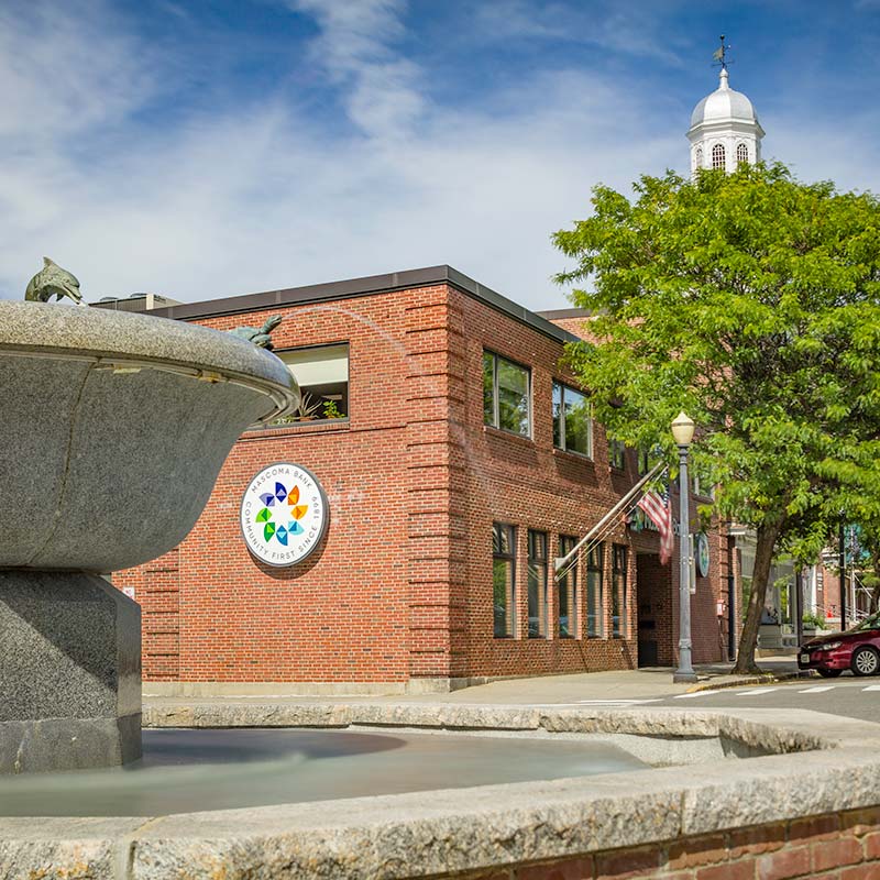 Red brick building with Mascoma logo on side of building. American Flag hanging in front