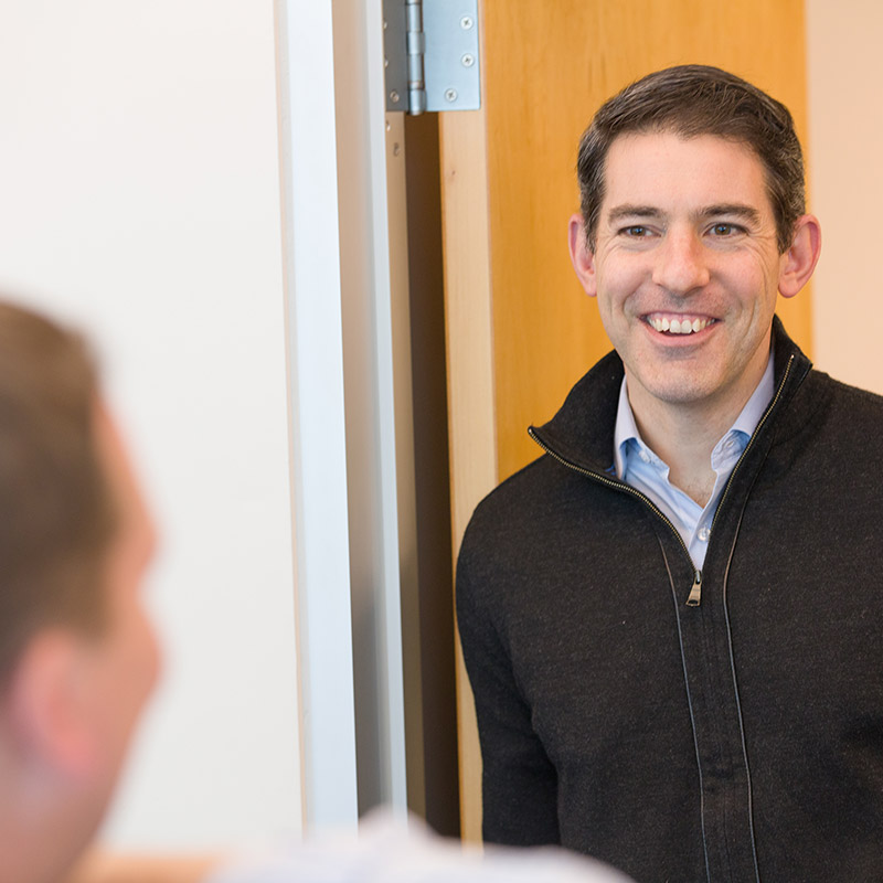 helpful bank employee wearing black pullover fleece leaning in a doorway smiling at customer