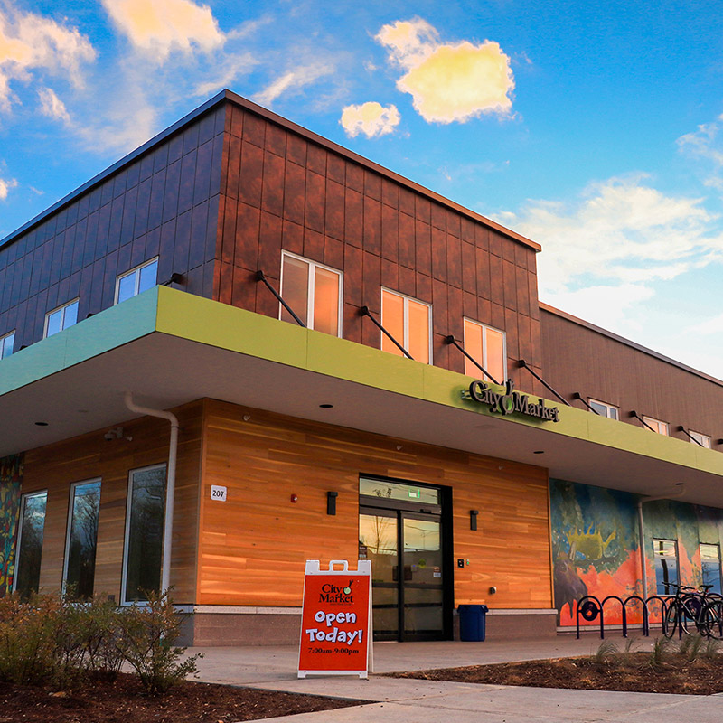 Storefront of a new City Market location supported by Mascoma Bank Business loans. Sun shines on a luminated rich orange and brown two tone building.