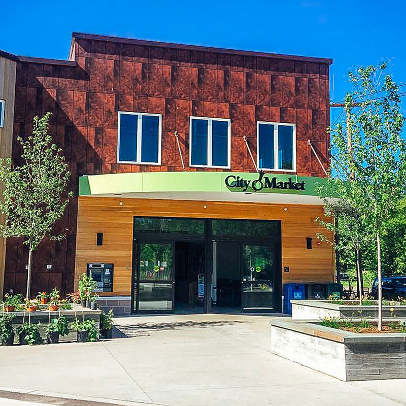 Storefront of a new City Market building financed by Macoma Bank. Cement walkway into a building flanked by young trees in front of a two toned building of brown and orange